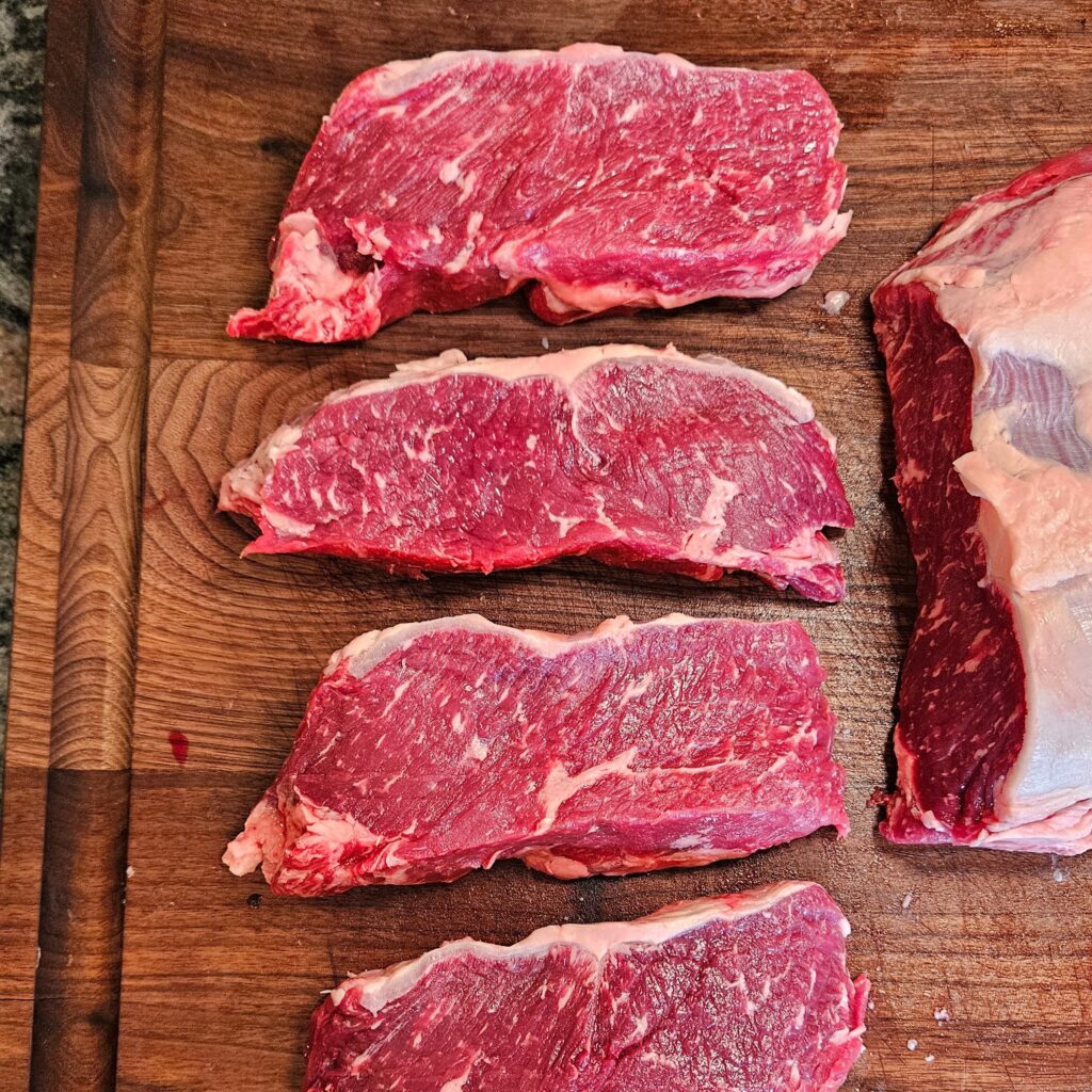 Raw cuts of ribeye steak on a wooden cutting board.