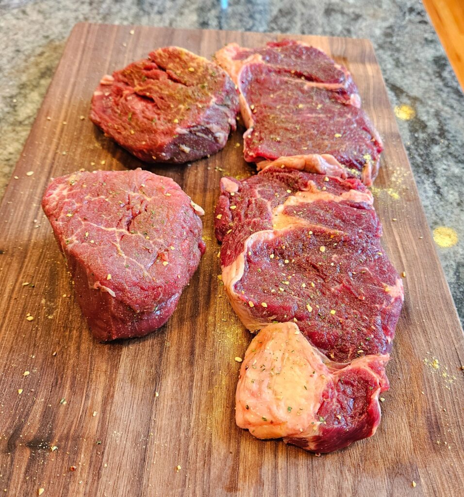 Seasoned Filet mignon and ribeye steak on a wooden board.