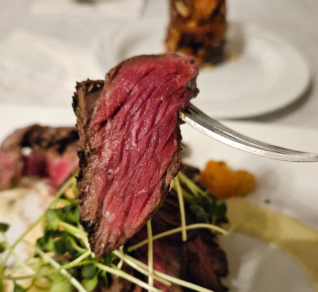 Close-up view of slice of medium rare steak on a fork.