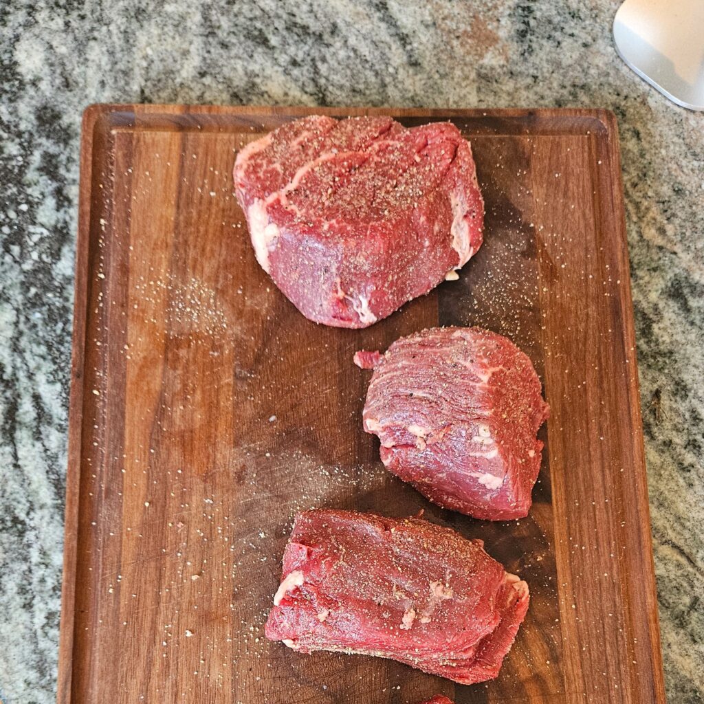 Seasoned filet mignon cuts on a wooden board on a table.