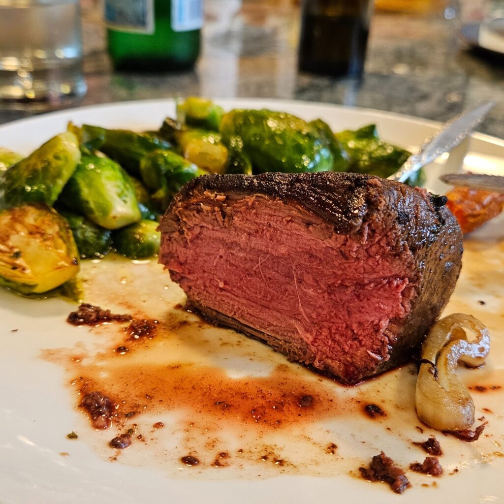 Filet mignon on a plate with roasted brussels sprouts.