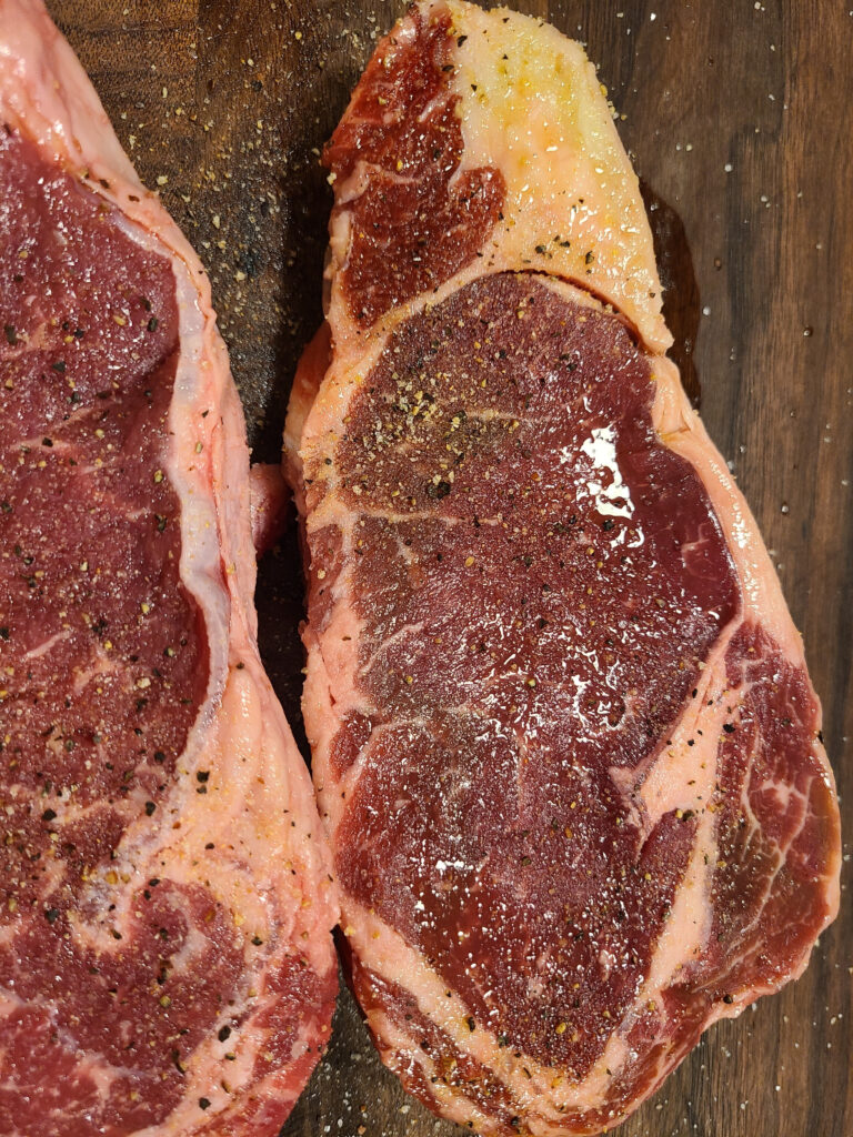 Close up of seasoned ribeye steak on a wooden board.