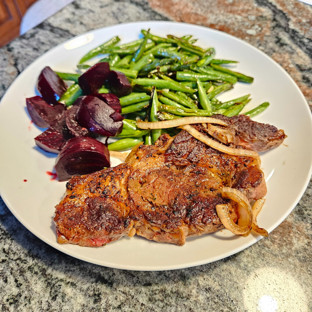 Ribeye steak with red onions and green beans on a plate on a table.