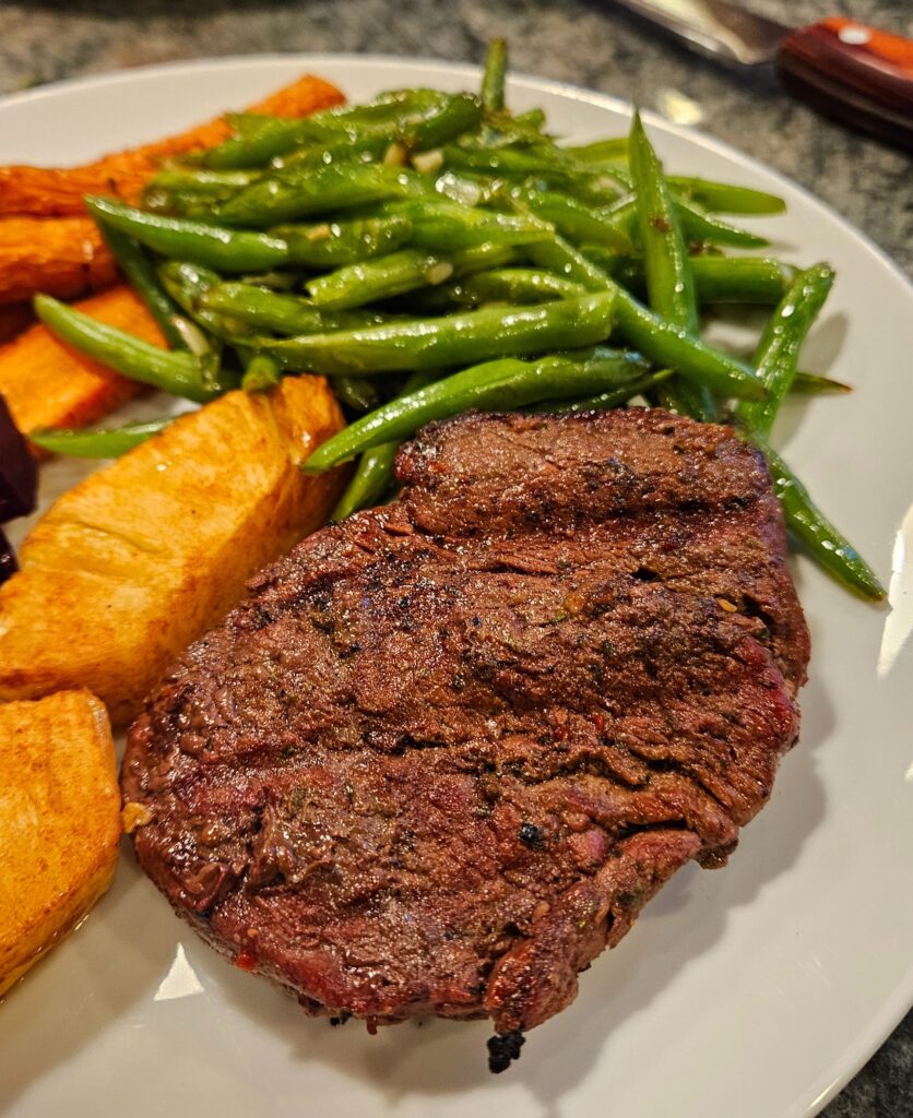 Ribeye steak with green beans and carrots on a plate.