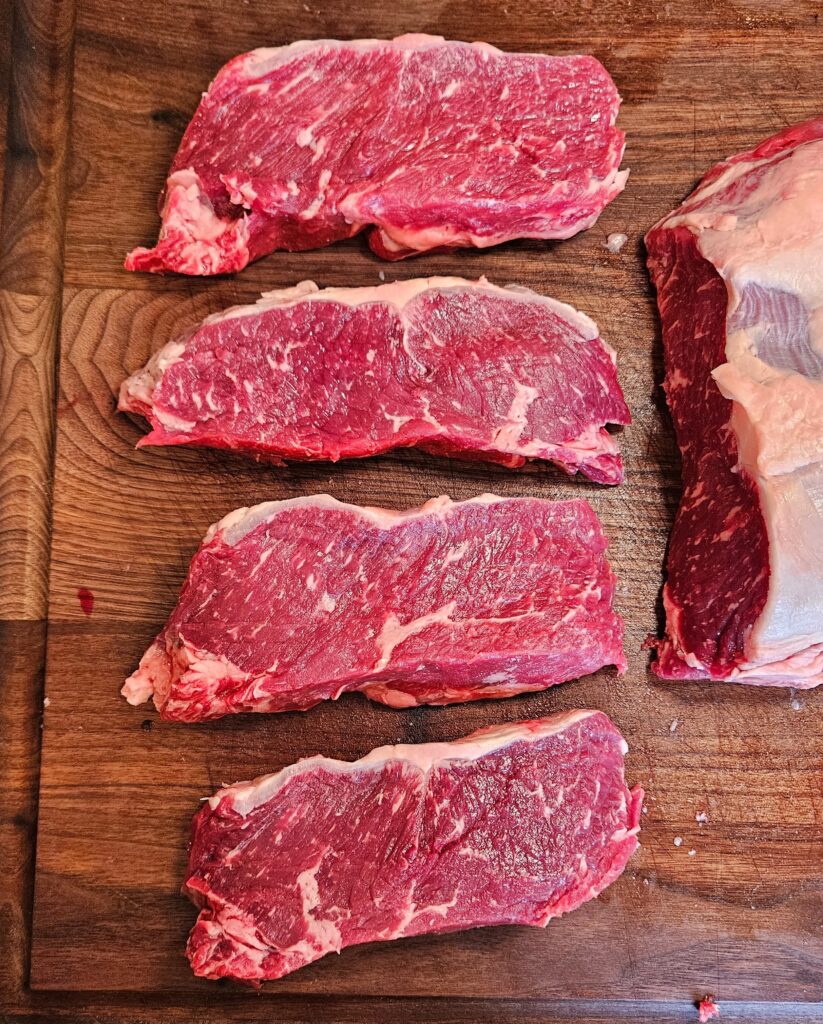 Raw ribeye cuts on a wooden board.