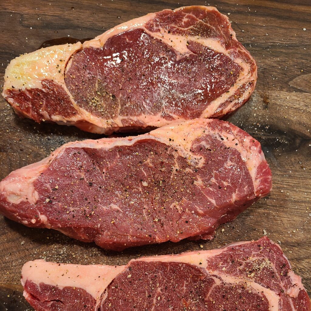 Seasoned ribeye steaks on a wooden board.