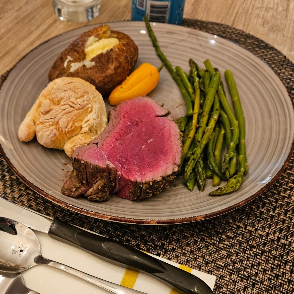 Prime rib on a plate with asparagus, bread, and potato.
