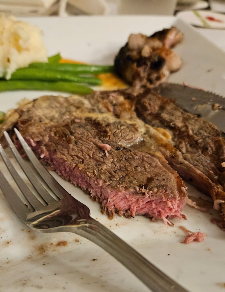Close up view of sliced medium ribeye steak with green beans and fork on a plate.