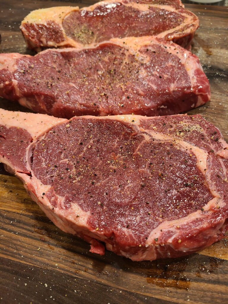 Seasoned ribeye steaks on a wooden board.