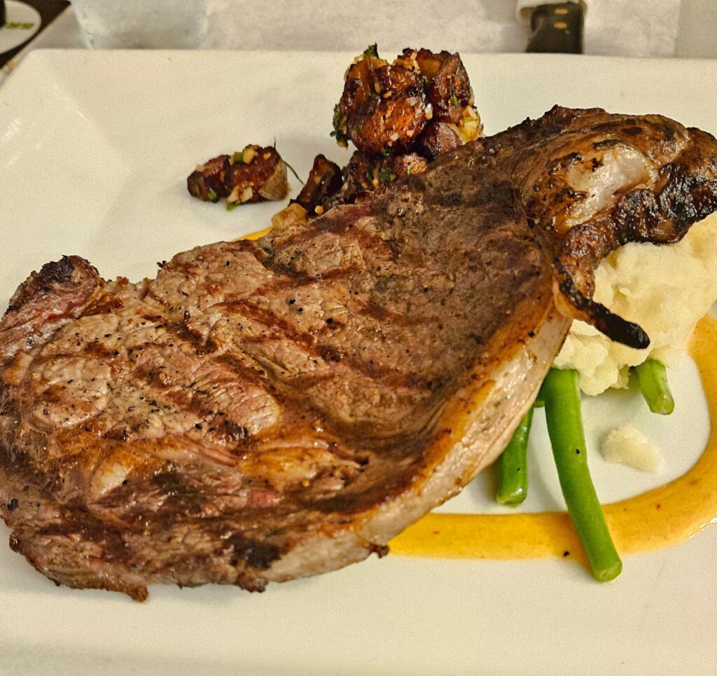 Ribeye steak on a plate with green beans and mashed potato.