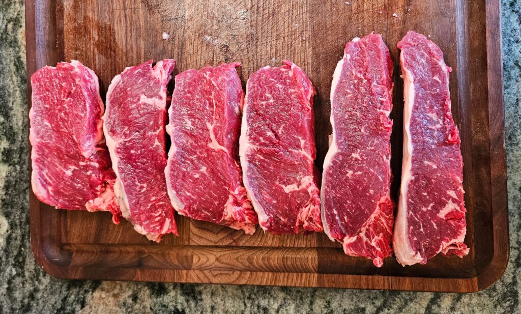 Cuts of steak on a wooden cutting board.