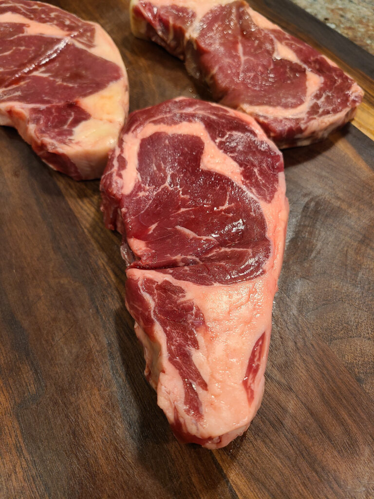 Cuts of raw ribeye steak on a wooden cutting board.