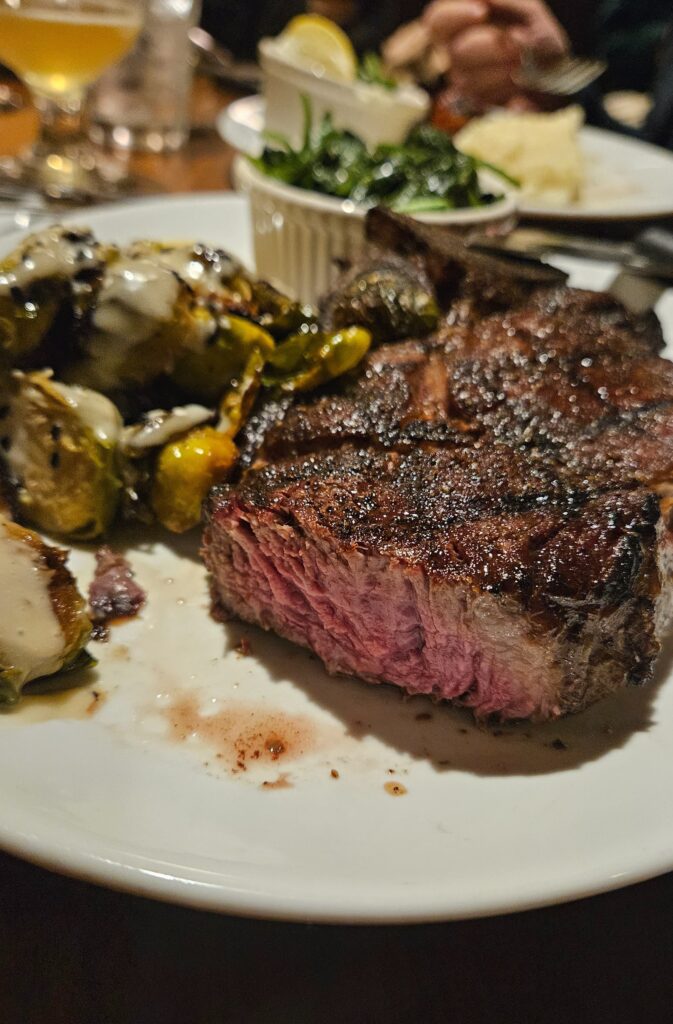 Medium rare ribeye steak on a plate with sides.