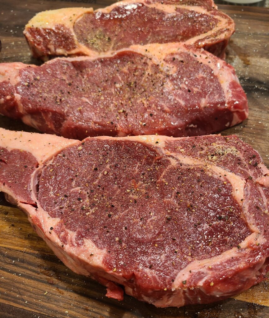 Seasoned ribeye steak cuts on a wooden board.