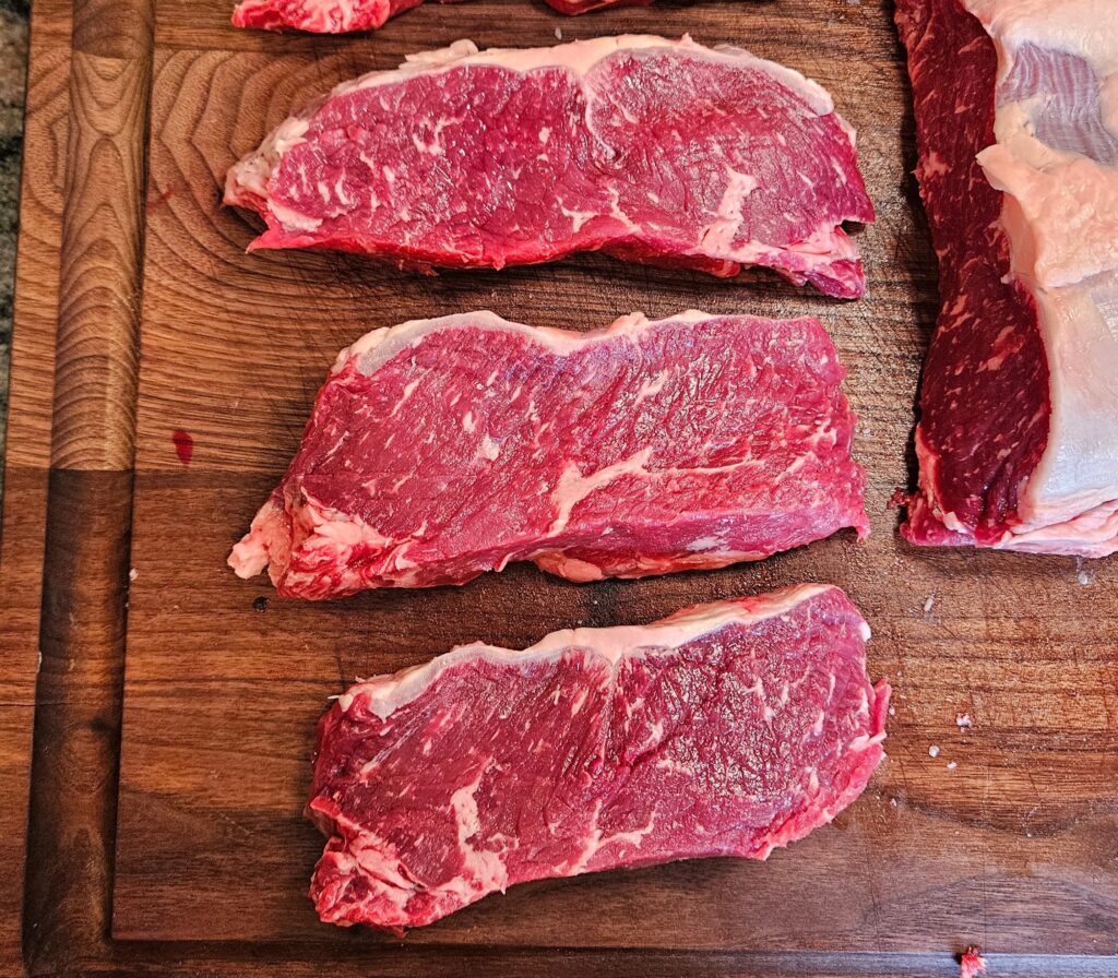Raw ribeye steak cuts on wooden board.