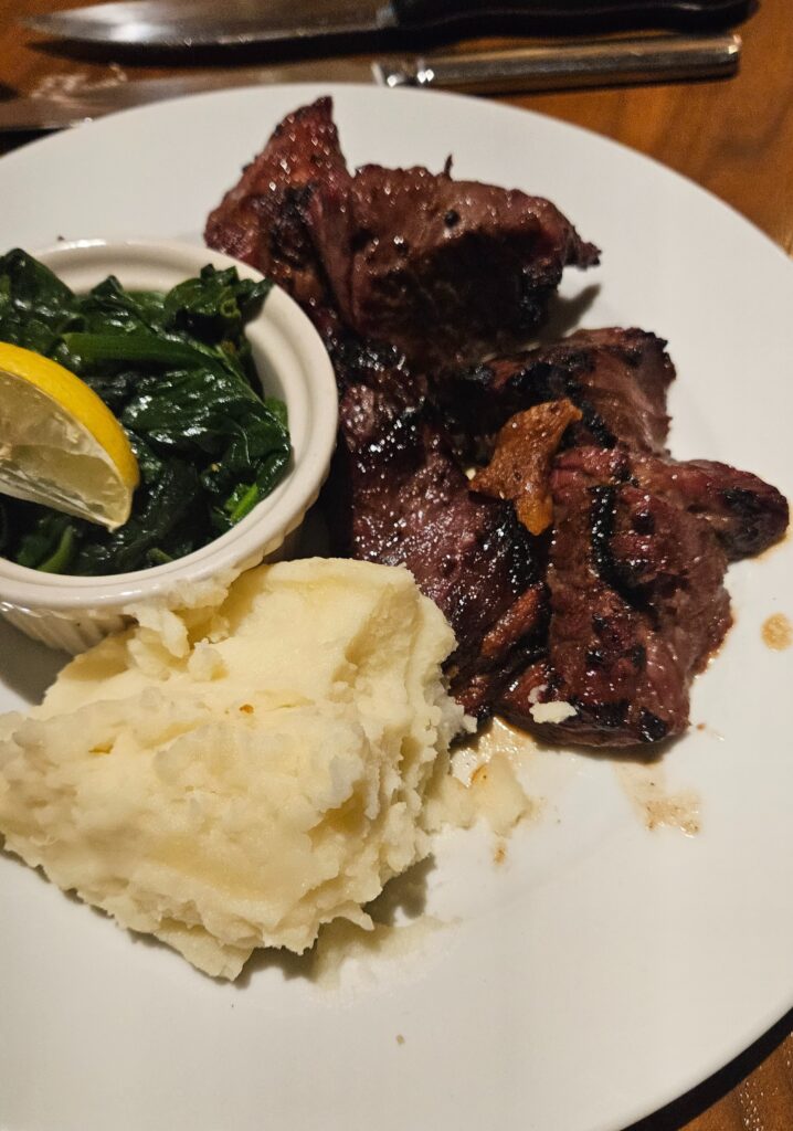 Ribeye steak with mashed potatoes and bowl of spinach on a plate.