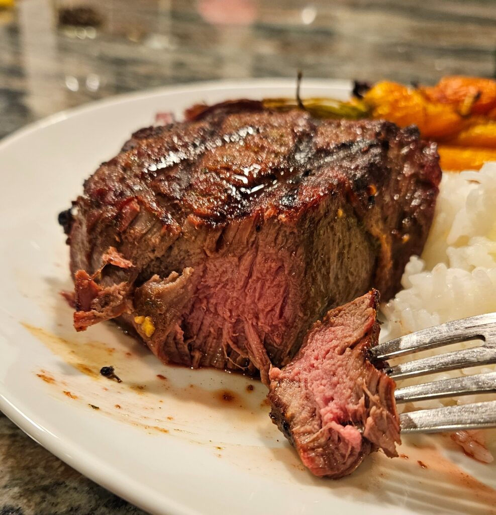 juicy filet mignon on a plate with rice and carrots with fork.
