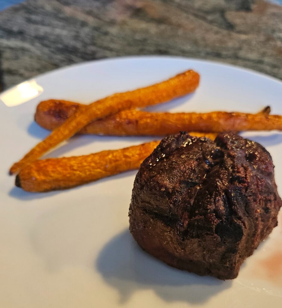 Filet mignon steak with roasted carrots on a plate.