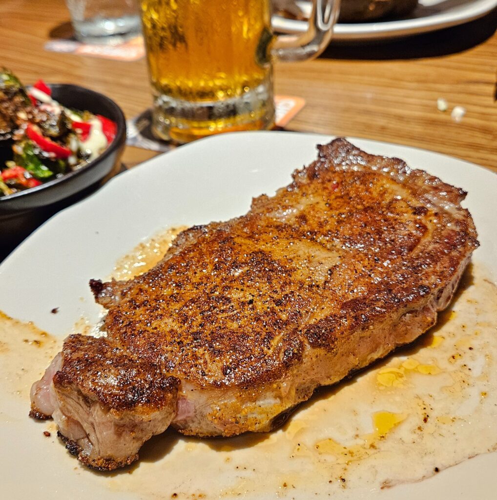 Grilled ribeye steak on a plate alongside a glass of beer.