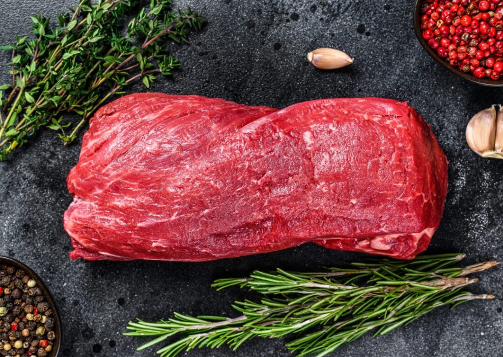Top view of raw cut of tenderloin surrounded by herbs and spices.