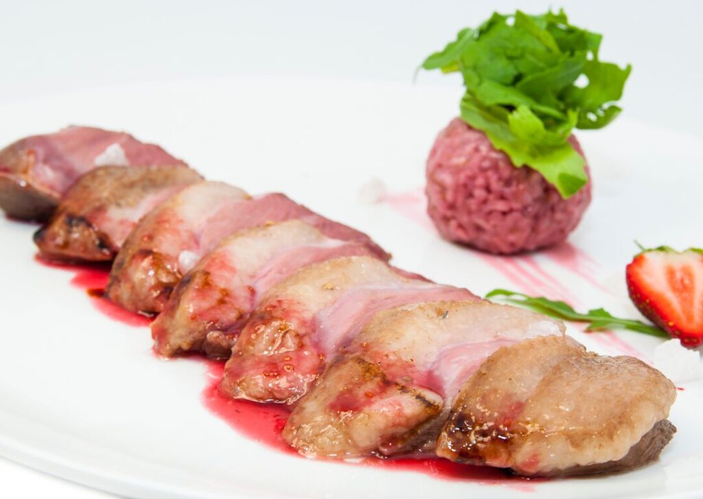 Roast goose meat on a plate with piece of strawberry.