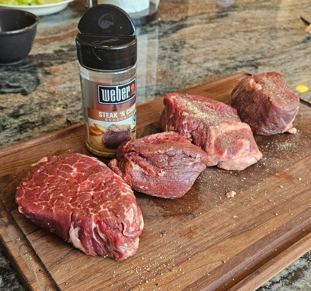 Cuts of filet mignon on a wooden board with steak seasoning.